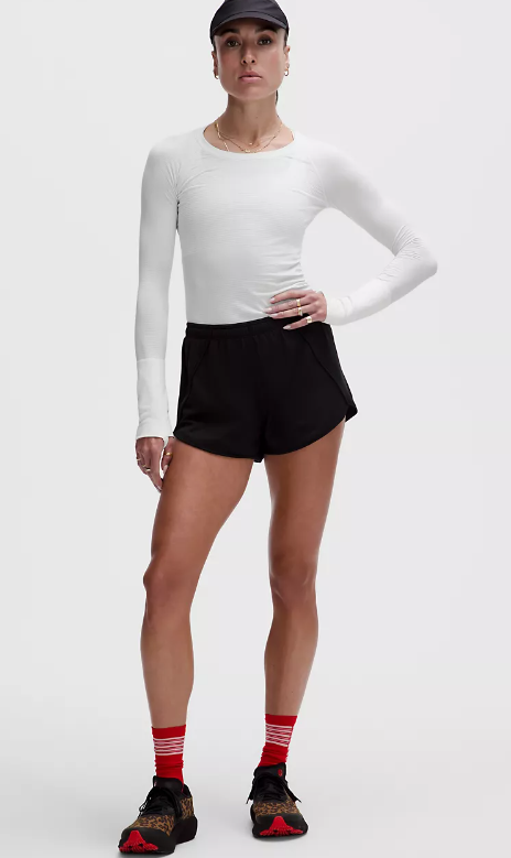 A woman wears a white long-sleeve top and black shorts.