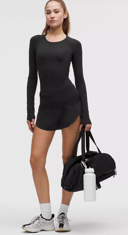 A woman wears a black long-sleeved athletic top and shorts.