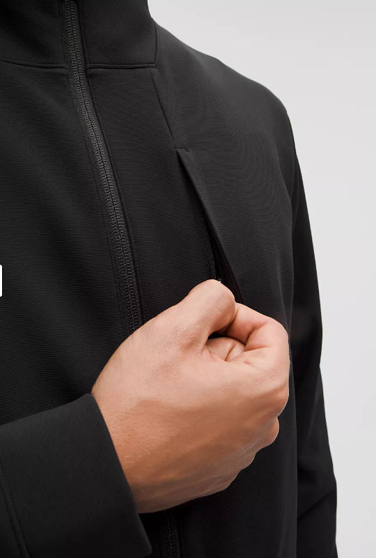 Black jacket with a zippered chest pocket being accessed by a hand.