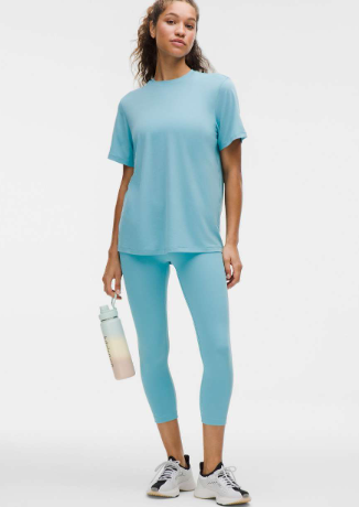 A woman in a blue short-sleeve training shirt and matching cropped leggings holds a water bottle.