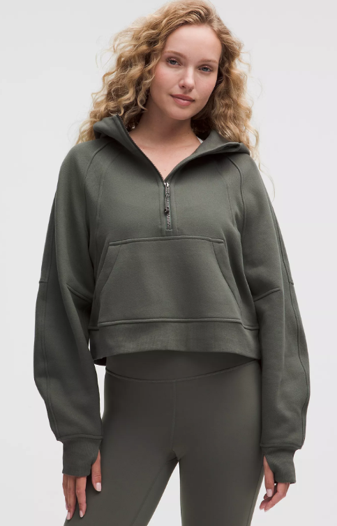 A woman wears a dark green oversized half-zip hoodie with a kangaroo pocket.