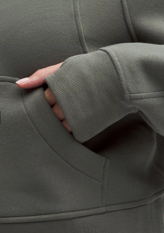 A hand rests in the pocket of a green oversized half-zip hoodie.