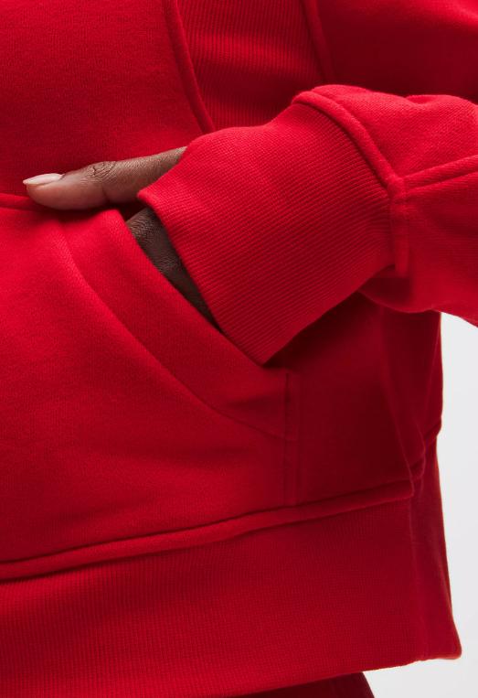 A close-up of a person's hand in the pocket of a red oversized half-zip hoodie.