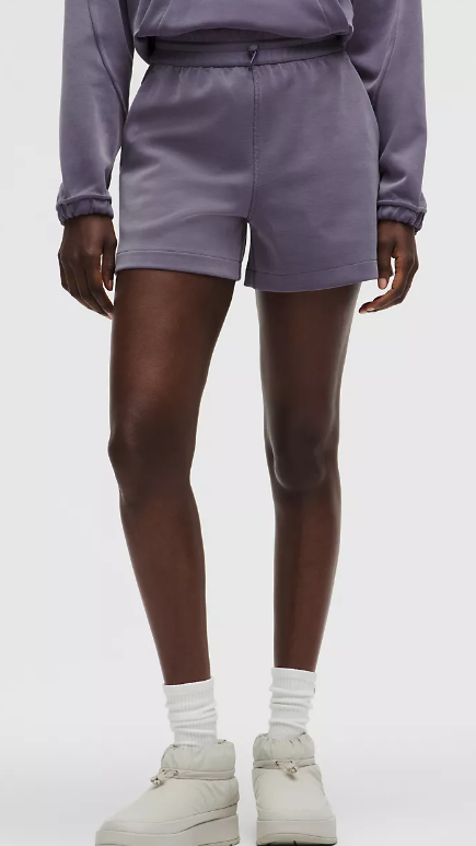 A person models grape mist colored high-rise shorts with white socks and light grey boots.