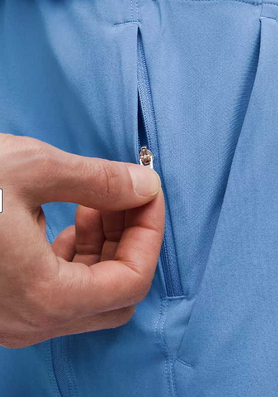 A hand zips open a pocket on blue athletic shorts.
