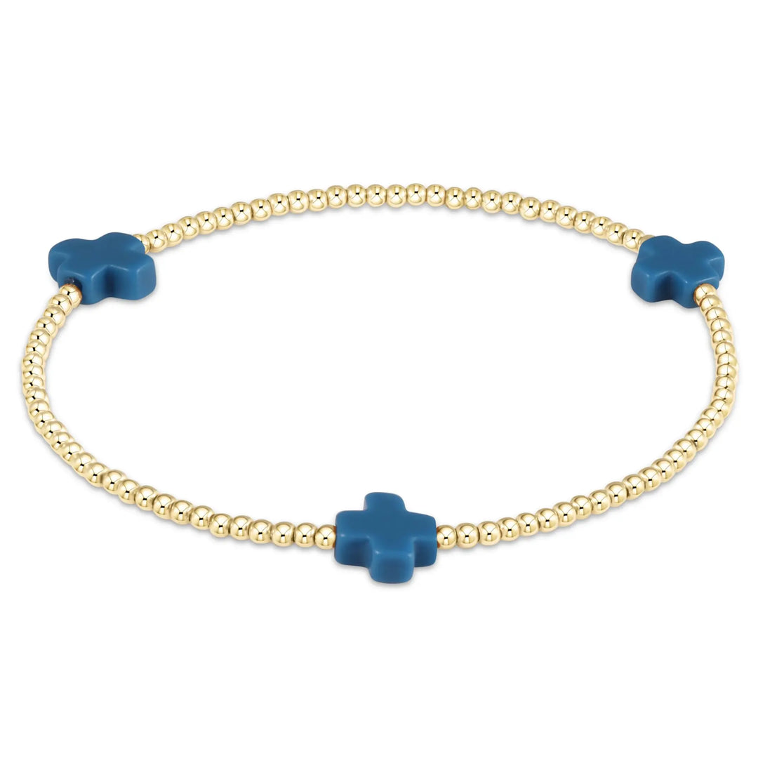 A gold beaded bracelet features three cobalt blue cross-shaped beads.
