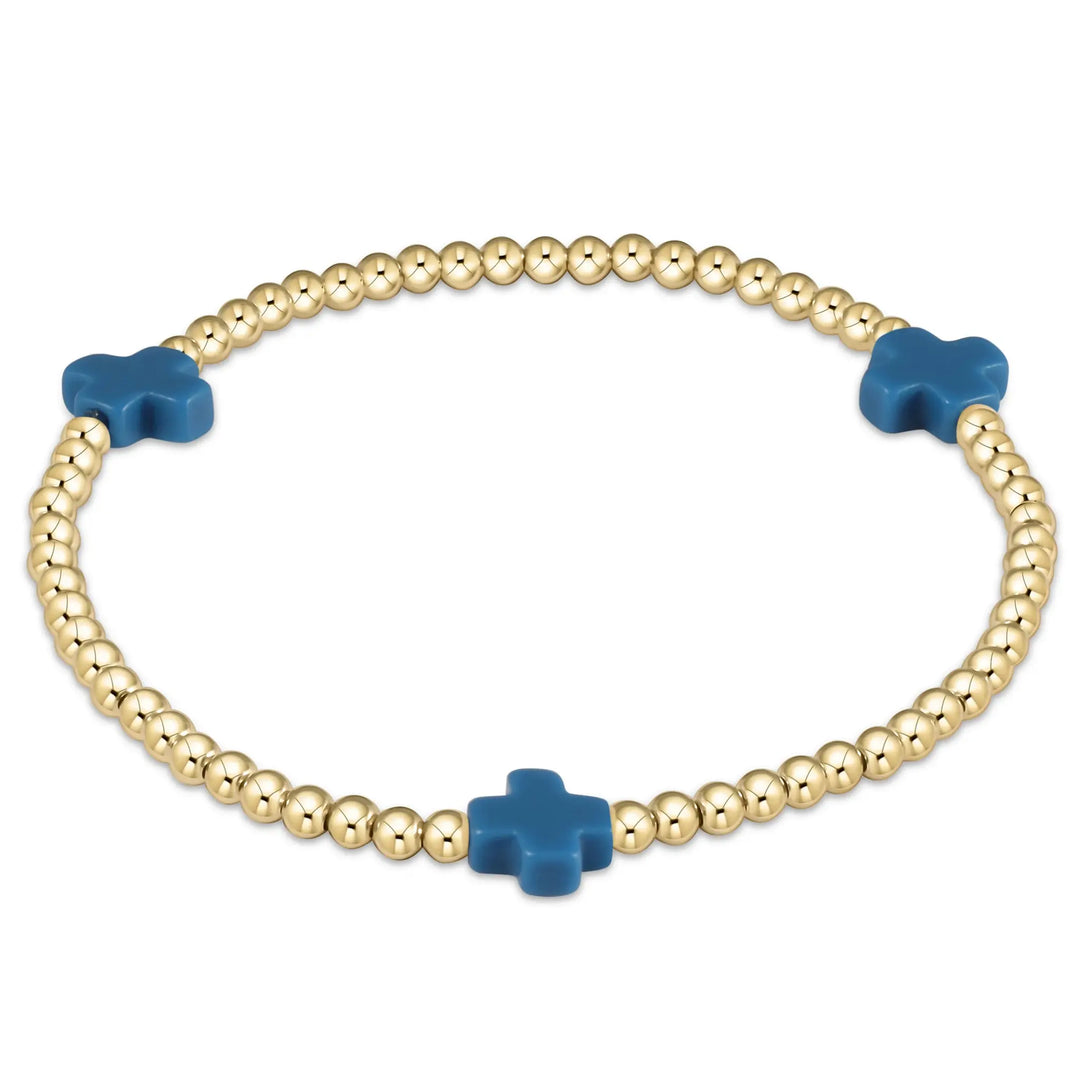 A gold beaded bracelet with three cobalt blue cross-shaped beads.