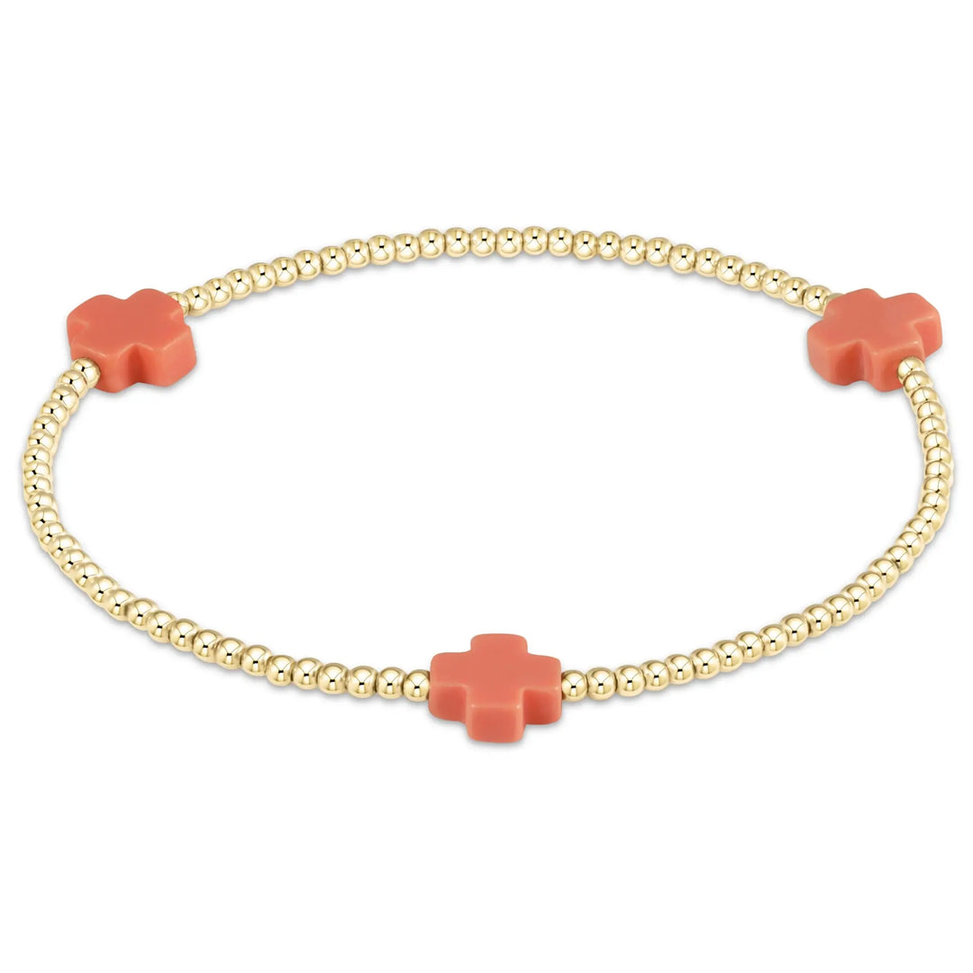 A gold beaded bracelet features three coral cross-shaped charms.
