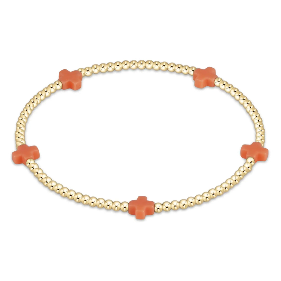 A gold beaded bracelet with five coral cross-shaped beads.