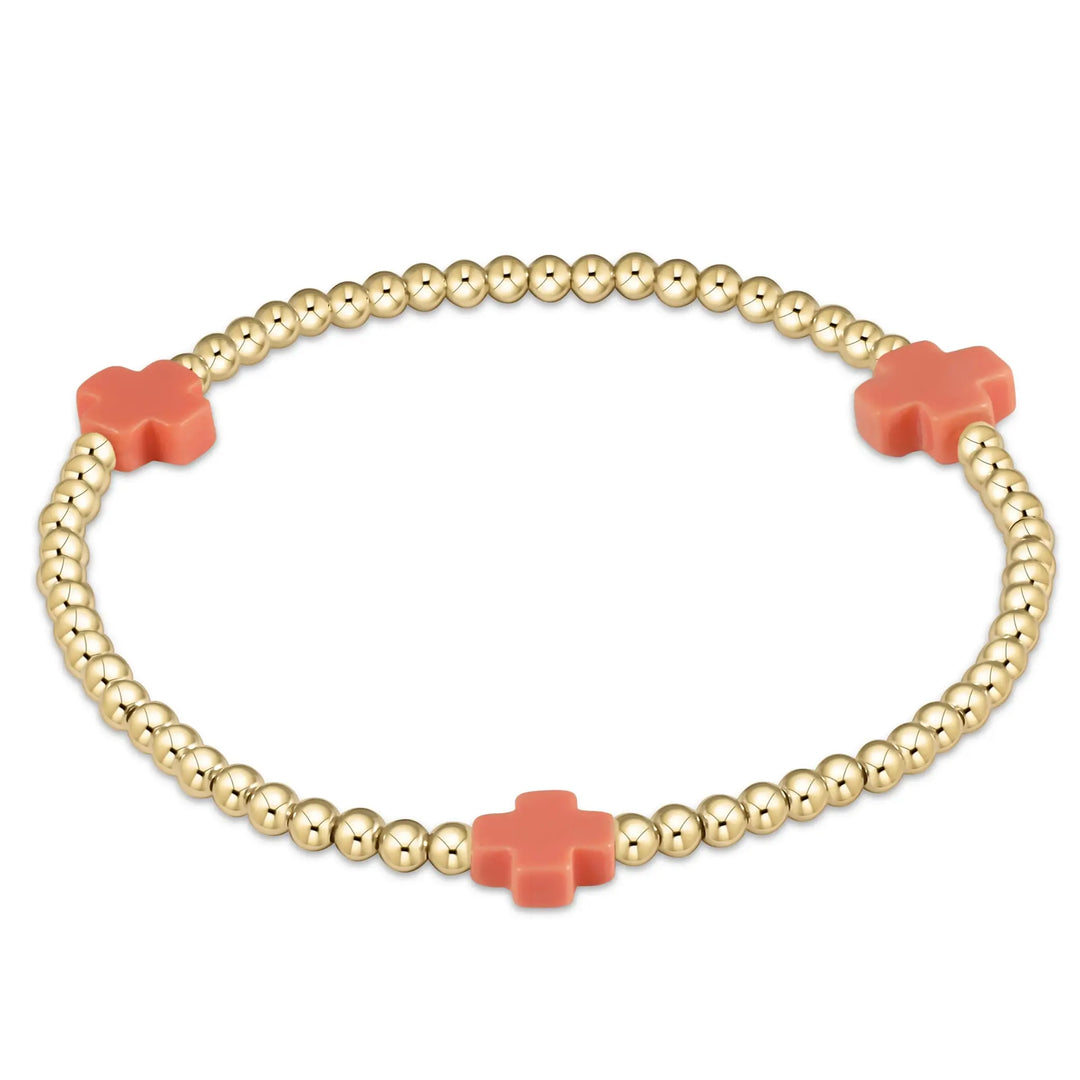 A gold beaded bracelet with three coral cross-shaped accents.