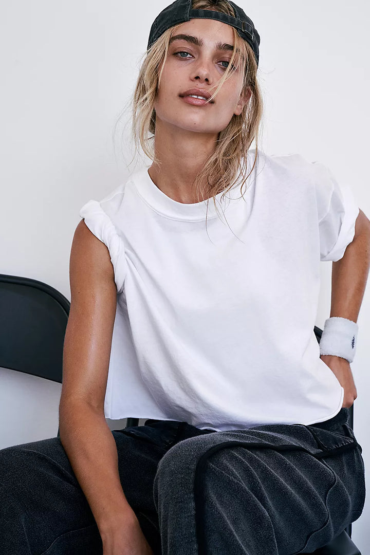 Inspire Tee Iss White: A woman in a white tee and black pants sits, wearing a black cap.
