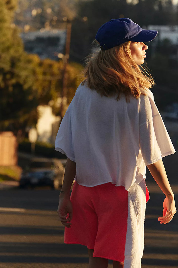 Inspire Tee Iss White, an oversized white tee with raw-edge seaming and coral shorts.