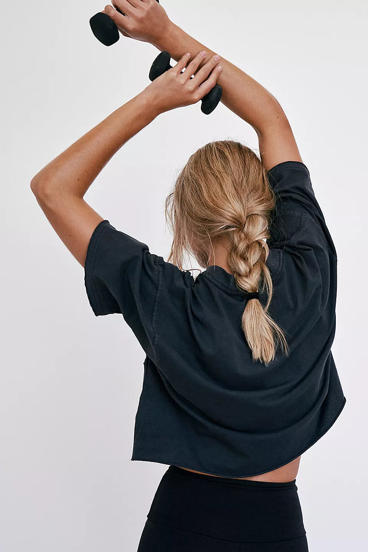 A woman in a black cropped tee with a braided ponytail holds two small weights.