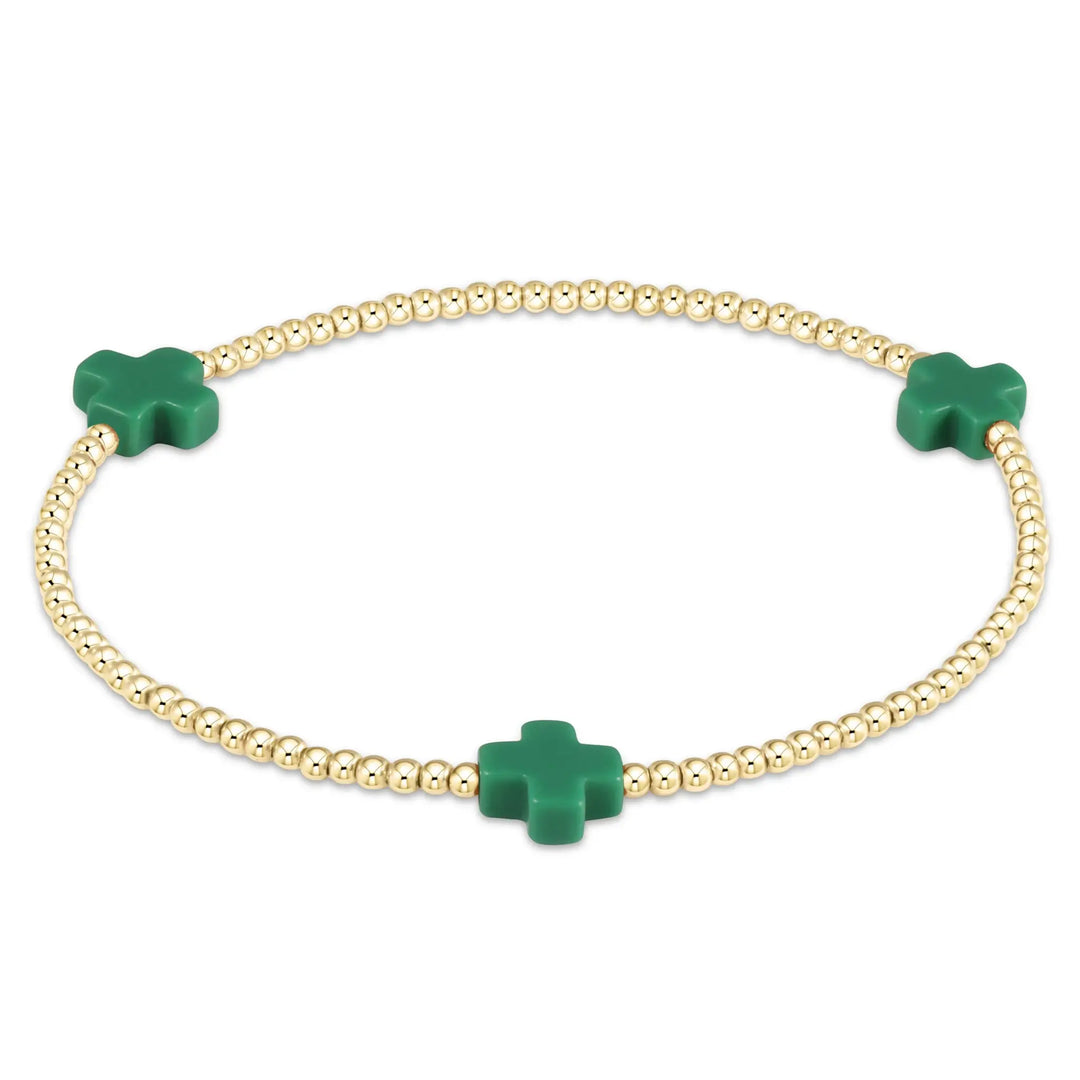 A gold beaded bracelet with three emerald green cross-shaped beads.