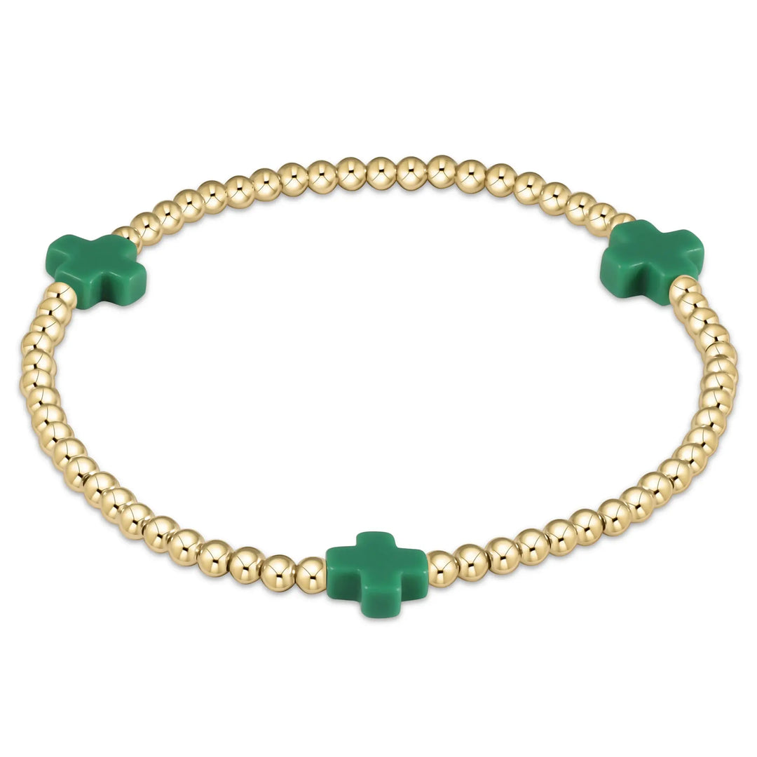 A gold beaded bracelet with three emerald green cross-shaped beads.