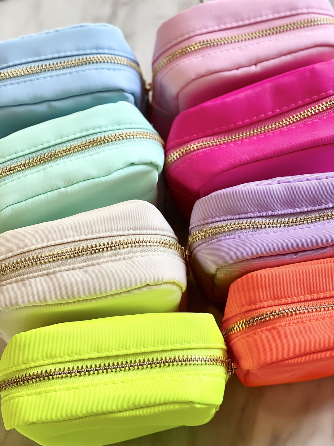 A collection of small nylon pouches in various pastel and neon colors with gold zippers.