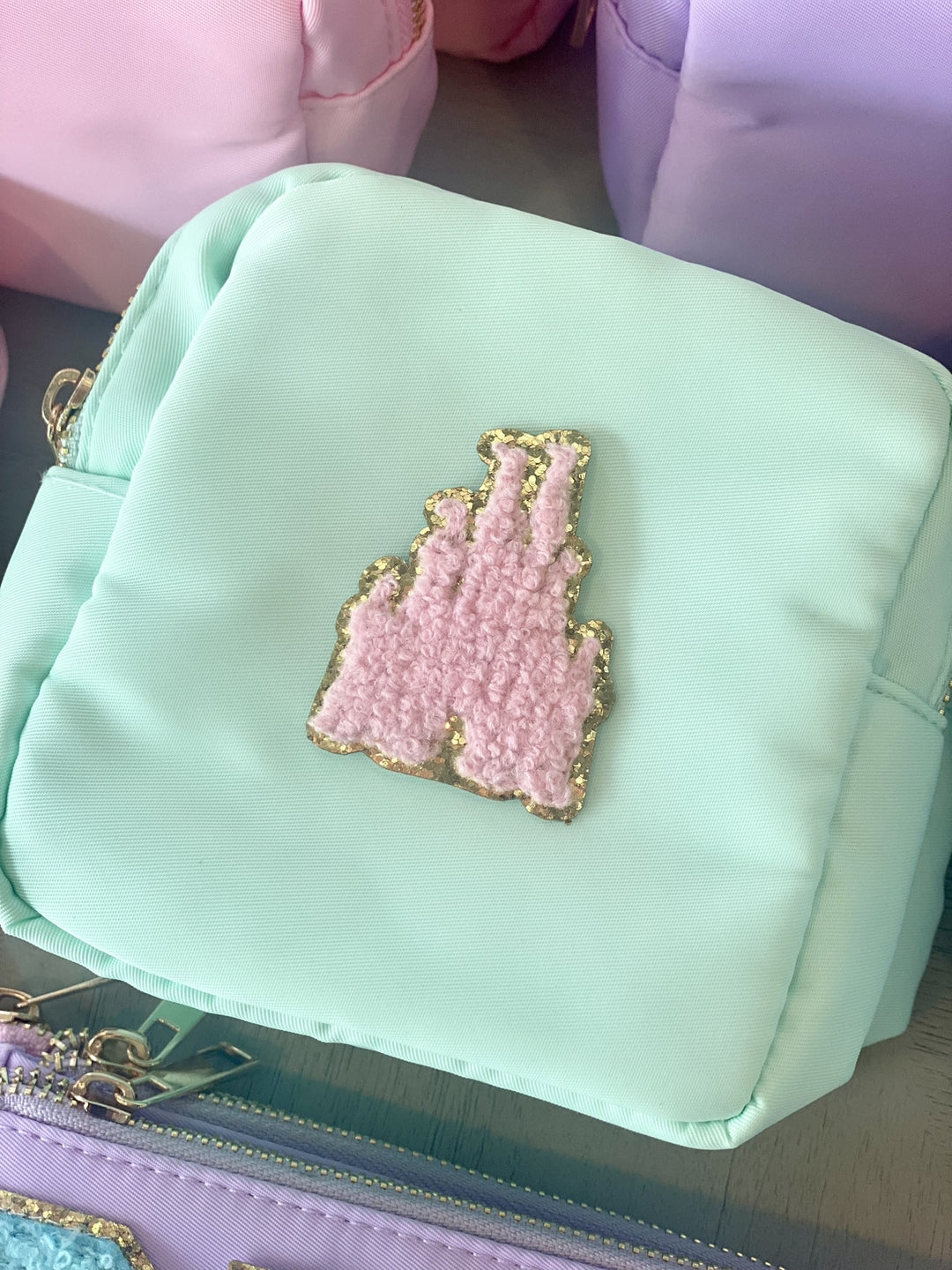 A mint green nylon pouch with a pink fuzzy castle patch outlined in gold glitter.