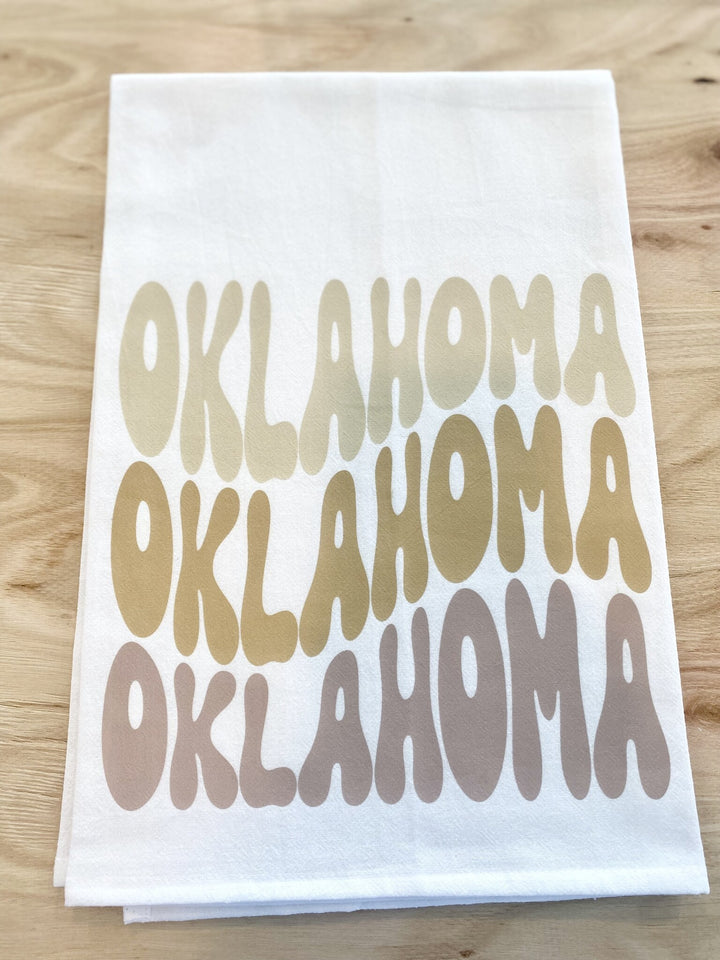 Neutral Oklahoma tea towel with "Oklahoma" printed three times in varying shades of brown.