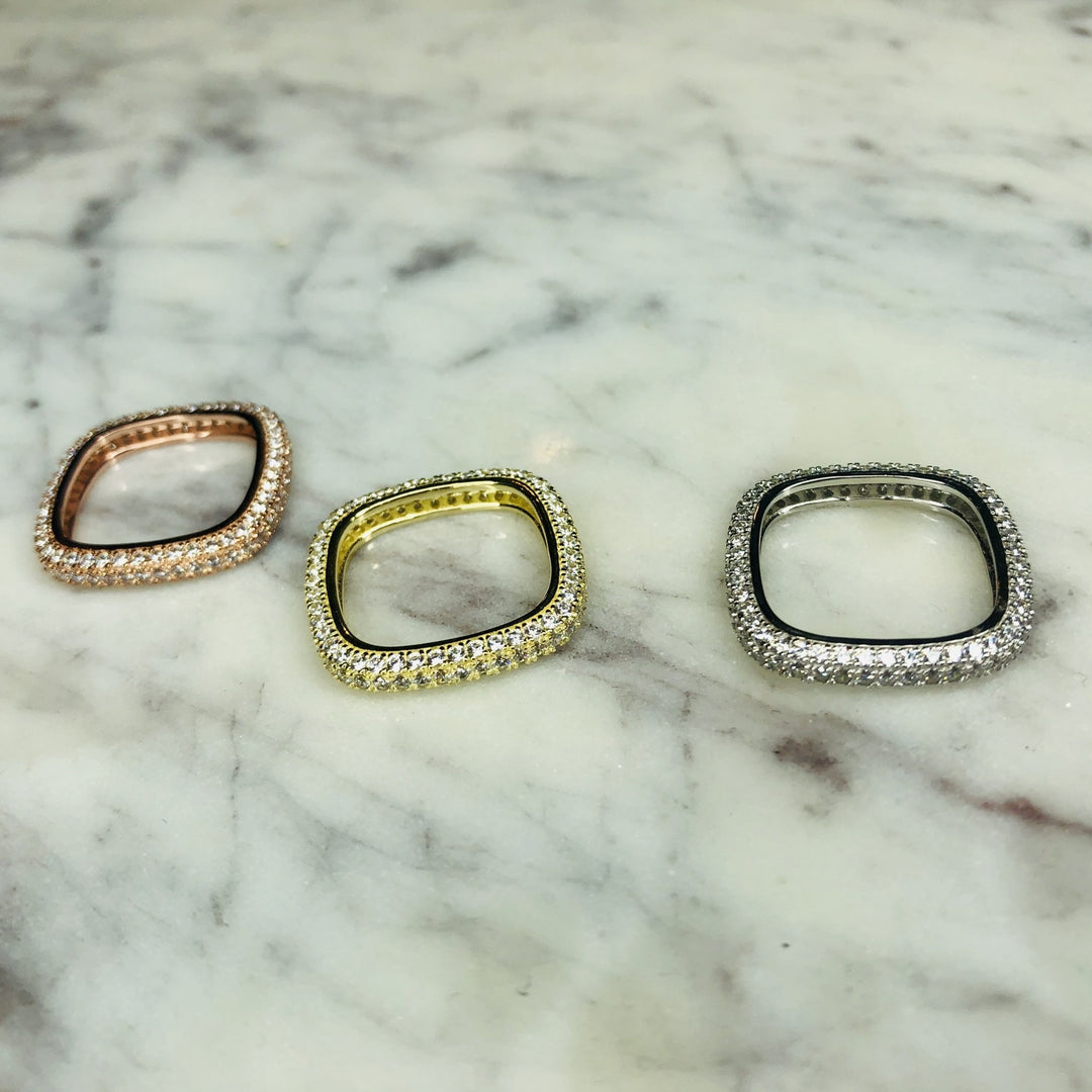 Three thin pave rings, one rose gold, one yellow gold, and one silver, on a marble surface.