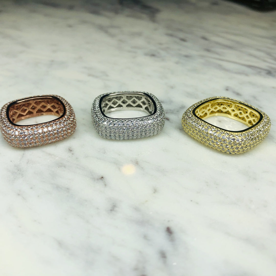 Three thick pave rings, one rose gold, one silver, and one gold, sit on a marble surface.