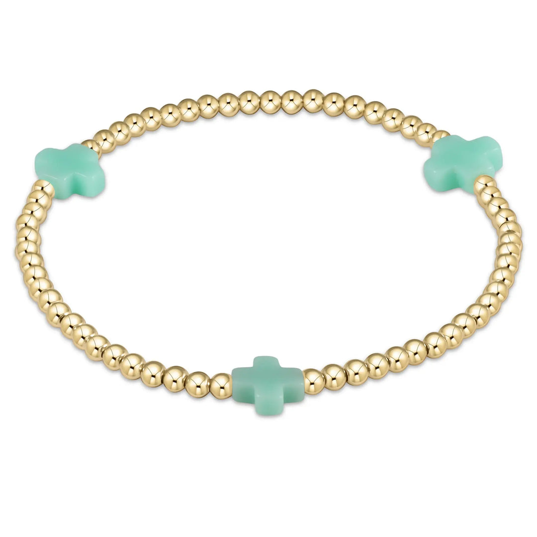 A gold beaded bracelet with three mint green cross-shaped beads.