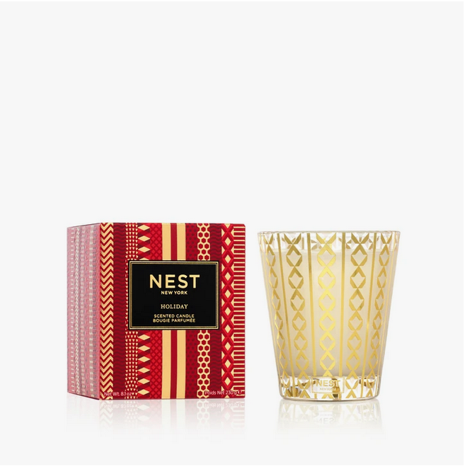 A Nest New York Holiday Classic Candle in a red and gold patterned box next to a gold-patterned glass candle.
