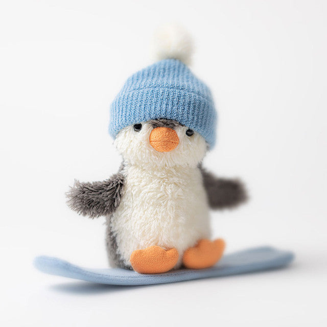A plush penguin wearing a blue beanie with a pom-pom stands on a blue snowboard.