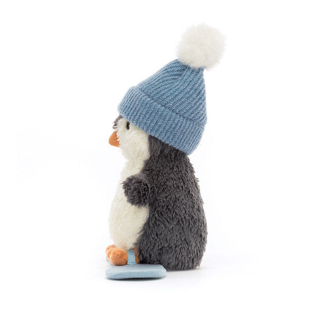 A plush penguin wearing a blue knitted hat with a pom-pom, standing on a blue snowboard.