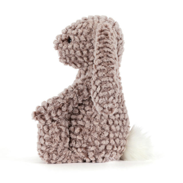 A plush, textured brown bunny with long ears and a white fluffy tail sits facing left.