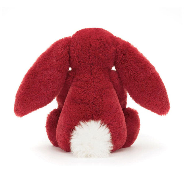 A red plush bunny with long ears and a white fluffy tail sits facing away.