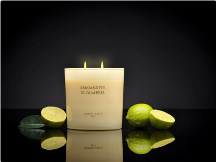 A lit ivory candle with three wicks, labeled "Bergamotto di Calabria," sits next to limes.
