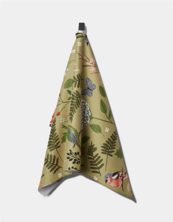 A green tea towel with a pattern of birds, butterflies, and foliage hangs from a hook.