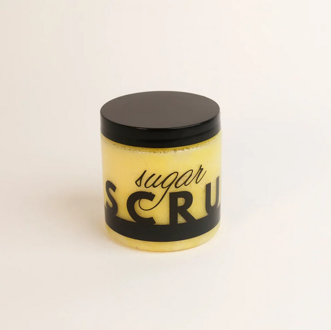 A yellow sugar scrub in a clear jar with a black lid and label.