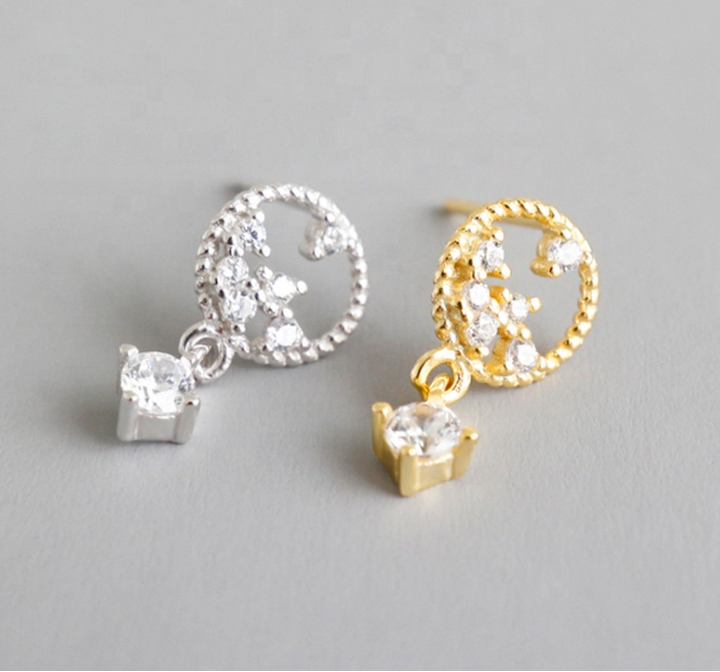 Two drop stud earrings, one silver and one gold, each featuring a crescent moon design with small clear stones and a larger clear stone dangling below.