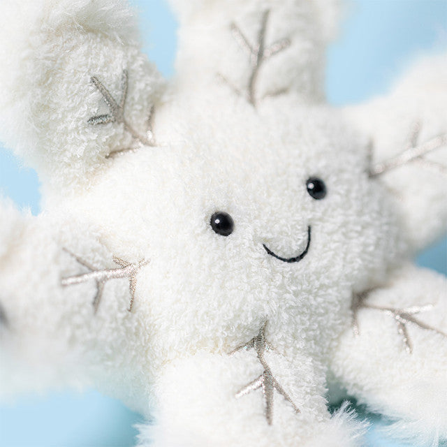 A plush white snowflake toy with a smiling face and embroidered details.
