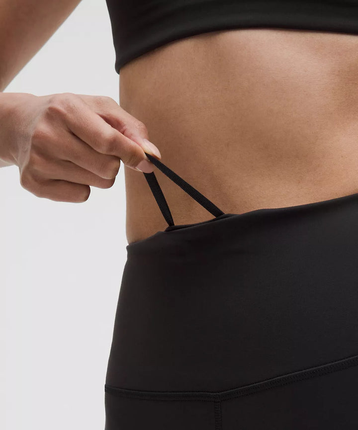 Close-up of black high-rise leggings with a hand adjusting the internal drawstring.