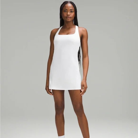 A woman models a white, sleeveless, A-line tennis dress with a square neckline.
